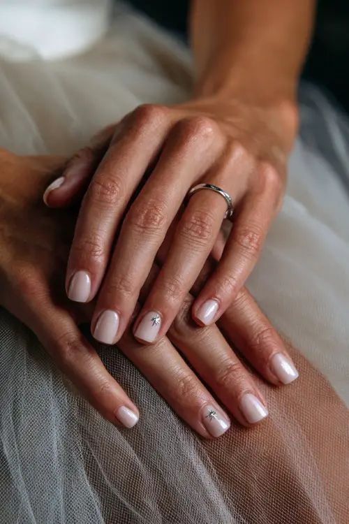 Close-up of bride’s hand resting on a tulle skirt, short square nails in soft ivory with glossy finish and tiny silver star accents on two fingers 