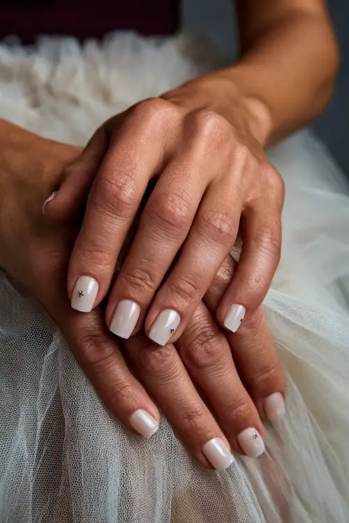 Close-up of bride’s hand resting on a tulle skirt, short square nails in soft ivory with glossy finish and tiny silver star accents on two fingers