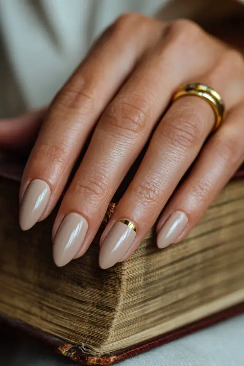 Close-up of bride’s hand resting on a vintage wedding book, soft beige almond nails with glossy finish and gold foil detailing on the ring finger