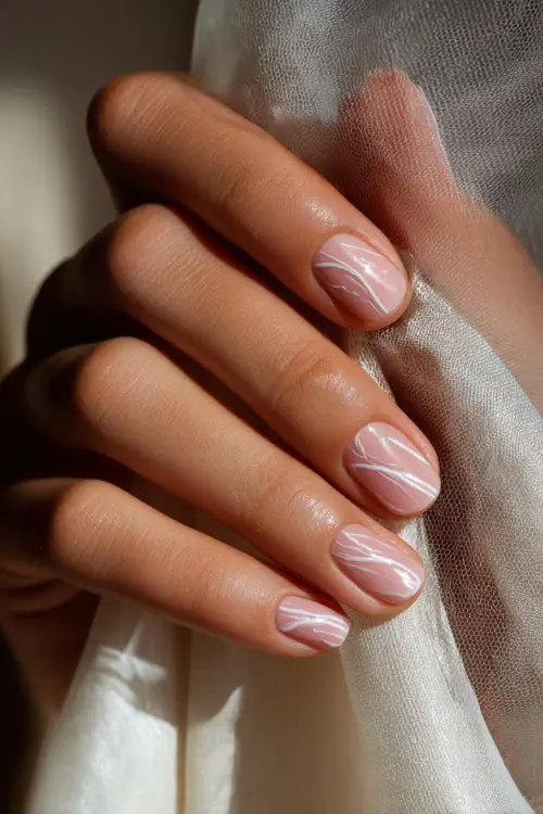 Close-up of bridesmaid’s hand helping with veil, soft beige-pink nails with thin white swirl art and glossy finish 