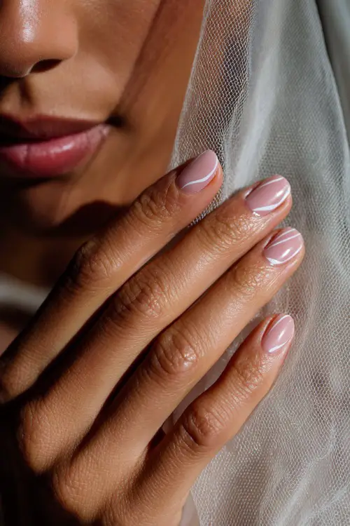 Close-up of bridesmaid’s hand helping with veil, soft beige-pink nails with thin white swirl art and glossy finish 