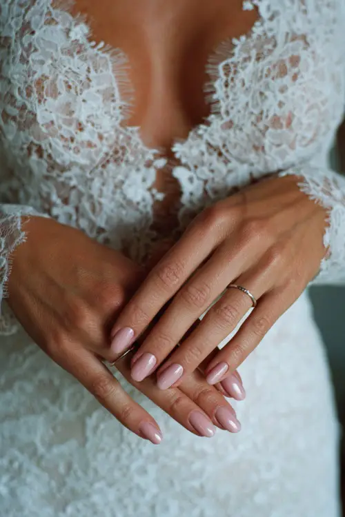 Close-up of elegant bride’s hands resting gently on a lace wedding dress, soft blush pink almond-shaped nails with delicate floral designs 