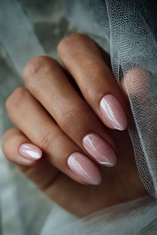 Close-up of fingers brushing through veil, almond nails in translucent pink with chrome shimmer and white swirl designs