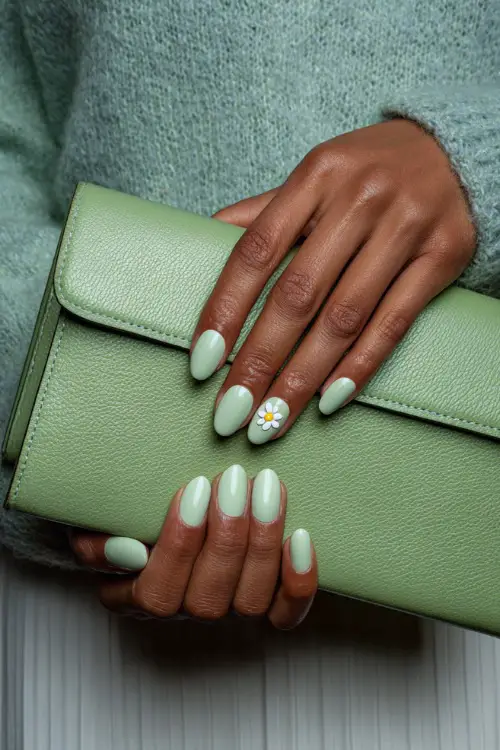Close-up of guest’s hand holding a light green clutch, almond-shaped nails in pastel mint green with glossy finish and one nail featuring a tiny white flower 