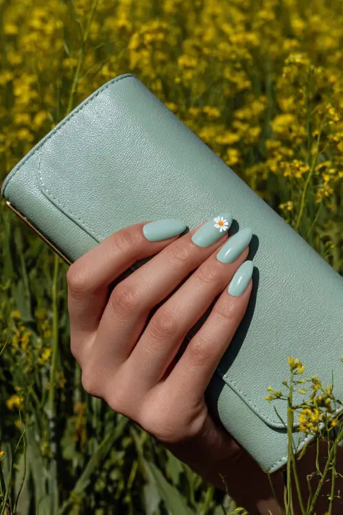 Close-up of guest’s hand holding a light green clutch, almond-shaped nails in pastel mint green with glossy finish and one nail featuring a tiny white flower 