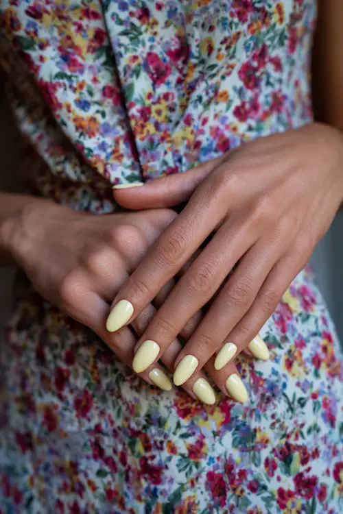 Close-up of guest’s hand on floral print dress, almond-shaped nails in pastel yellow with clear gloss and subtle white line detail on each nail 