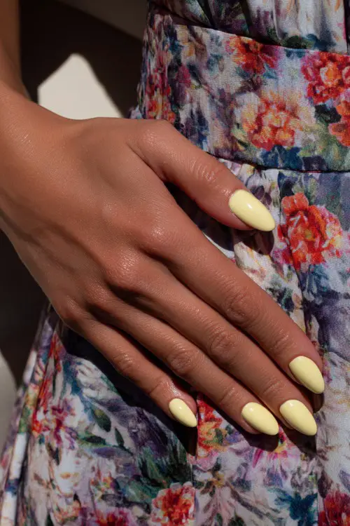 Close-up of guest’s hand on floral print dress, almond-shaped nails in pastel yellow with clear gloss and subtle white line detail on each nail