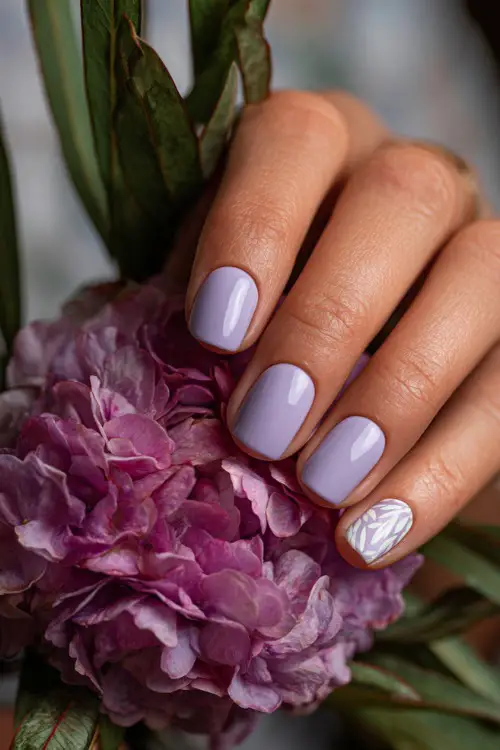 Close-up of hand adjusting a floral crown, short square nails in soft pastel lilac with a subtle chrome shine and one accent nail in white leaf pattern