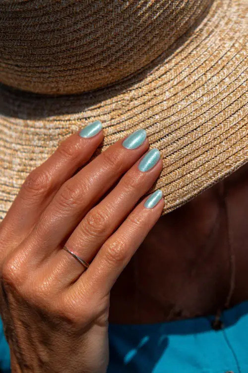 Close-up of hand adjusting a sun hat, almond nails in pastel mint with fine iridescent shimmer and white swirl detailing