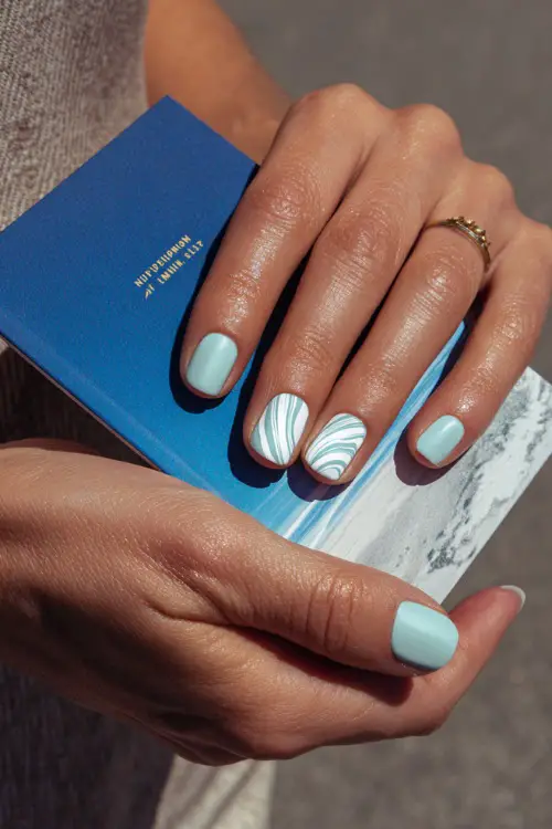 Close-up of hand holding a wedding program, short square nails in pastel mint with one accent nail featuring a white swirl design 