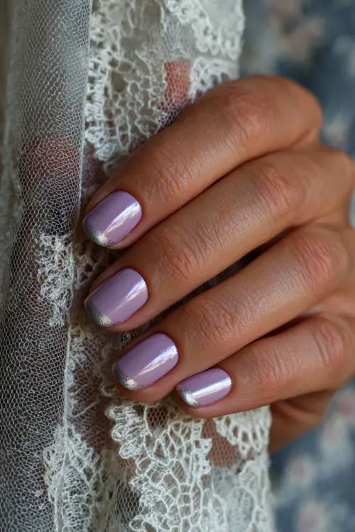 Close-up of hand holding lace-trimmed veil, ballerina-shaped nails in pastel lavender with chrome French tips and one accent nail in silver foil 