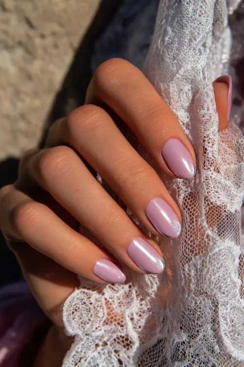 Close-up of hand holding lace-trimmed veil, ballerina-shaped nails in pastel lavender with chrome French tips and one accent nail in silver foil 