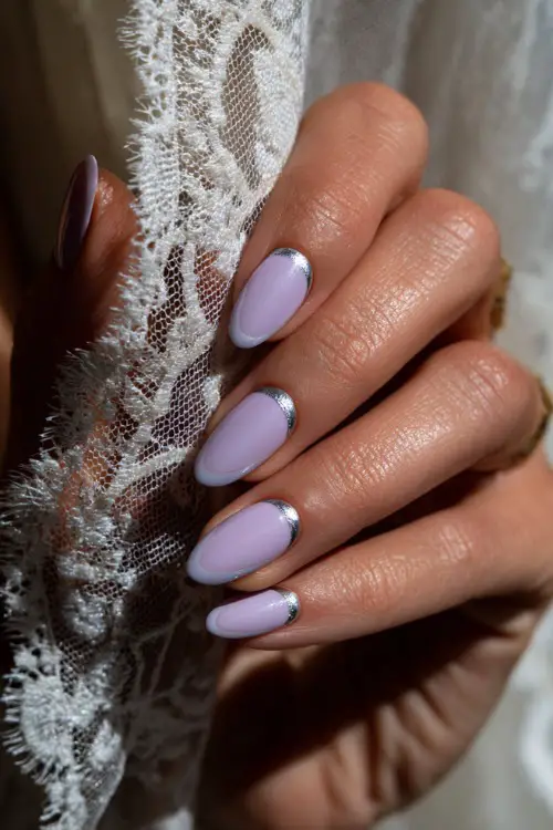 Close-up of hand holding lace-trimmed veil, ballerina-shaped nails in pastel lavender with chrome French tips and one accent nail in silver foil