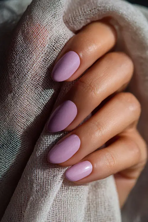 Close-up of hand holding sheer veil, medium almond nails in soft pastel lilac with chrome dust shimmer and clean edges 