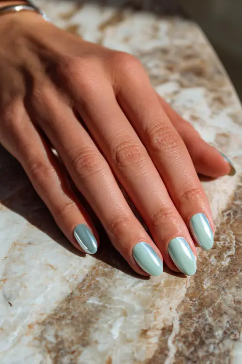 Close-up of hand laying on a marble table, short almond nails in pastel mint with chrome French tips and soft gloss 