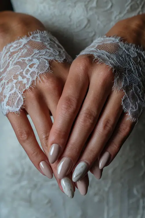 Elegant close-up of a bride holding lace gloves, featuring glossy ballerina nails in neutral beige with marble accent on middle fingers 