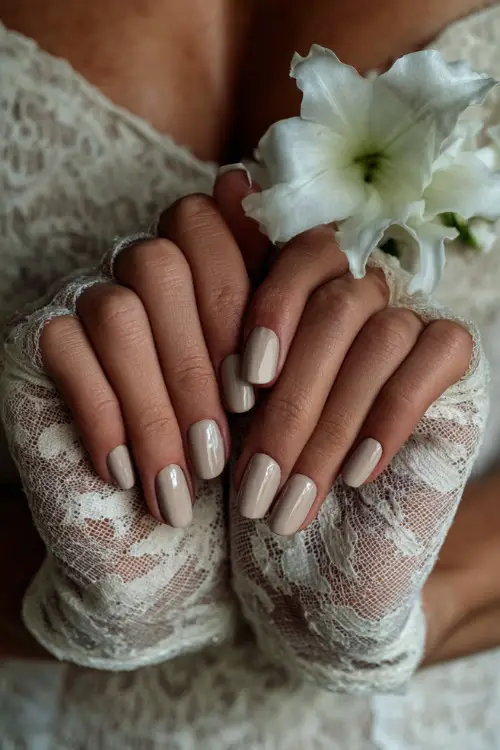 Elegant close-up of a bride holding lace gloves, featuring glossy ballerina nails in neutral beige with marble accent on middle fingers