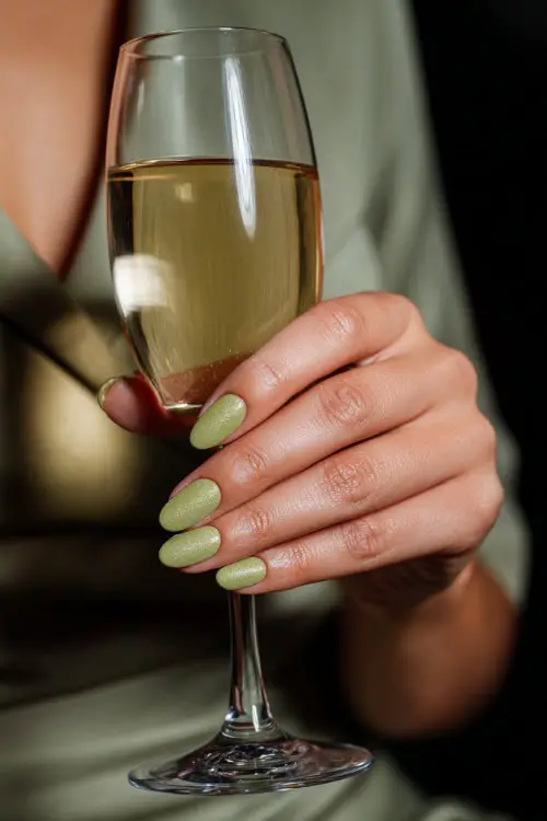 Elegant guest holding a champagne glass, medium oval nails in pistachio green with shimmer topcoat and silver dot detail at the cuticle 