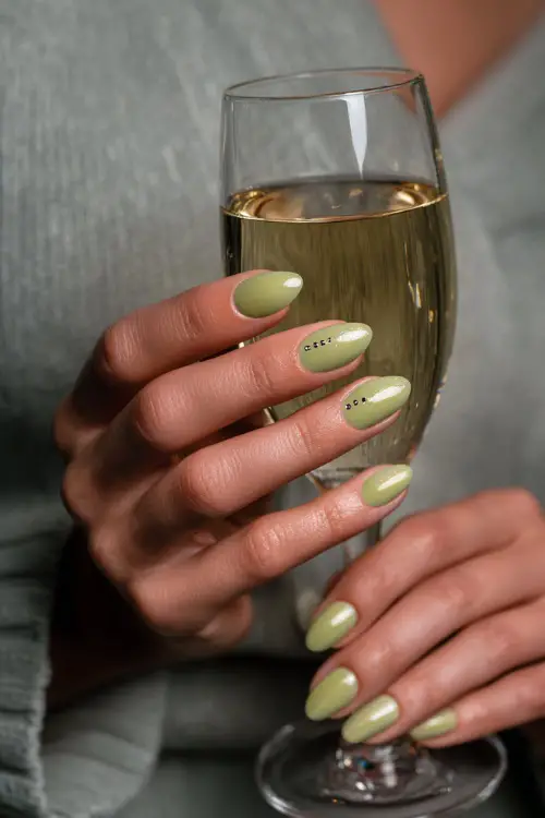 Elegant guest holding a champagne glass, medium oval nails in pistachio green with shimmer topcoat and silver dot detail at the cuticle