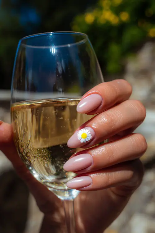 Elegant guest holding iced drink, short oval nails in soft blush pink with white daisies on the ring finger, sunny outdoor background