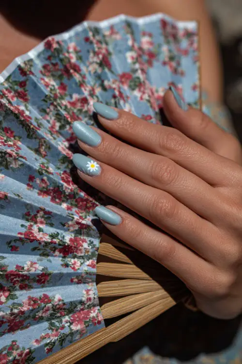 Elegant hand holding a floral-printed wedding fan, soft blue almond nails with sheer shimmer finish and a small daisy sticker on each ring finger