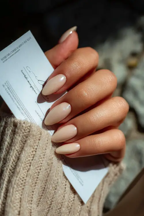 Elegant hand holding a wedding invitation, almond nails in creamy rose with pearl shimmer and delicate silver glitter arch near the cuticle