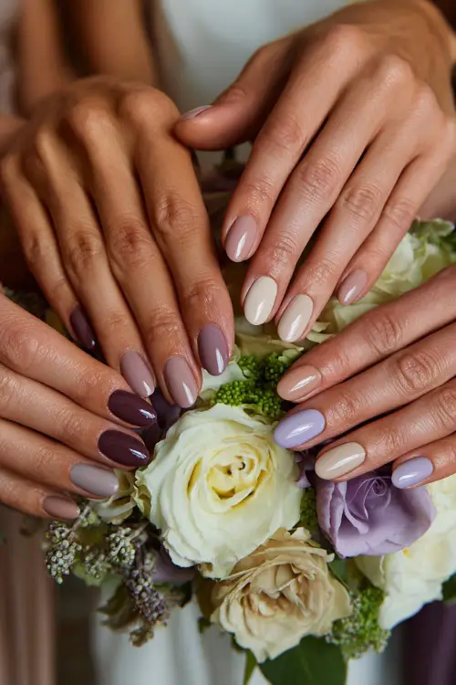 Group of bridesmaids’ hands reaching into a bouquet, coordinated nails in soft mauve, champagne shimmer, and pale lavender shades, mix of oval and round shapes 