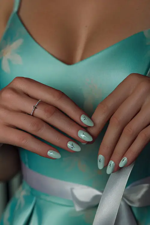Guest’s hand fixing a ribbon on her dress, medium almond nails in pastel jade with shiny topcoat and tiny silver star accents