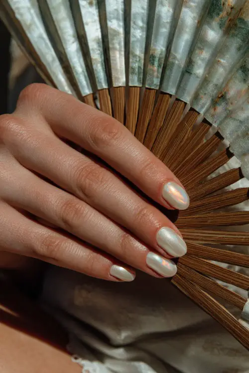 Guest’s hand holding a silk fan, short square nails in soft ivory with a matte finish and one nail featuring a tiny rose gold swirl