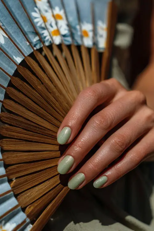 Guest’s hand holding a wedding program fan, rounded nails in soft pastel green with shimmer overlay and daisy petals painted on the thumb nail