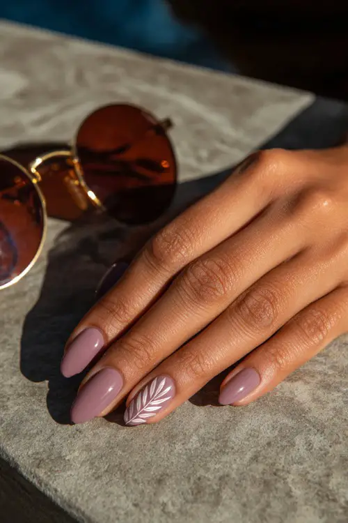 Guest’s hand placing sunglasses on a table, short almond nails in muted lavender with a glossy finish and one accent nail with leaf line art 