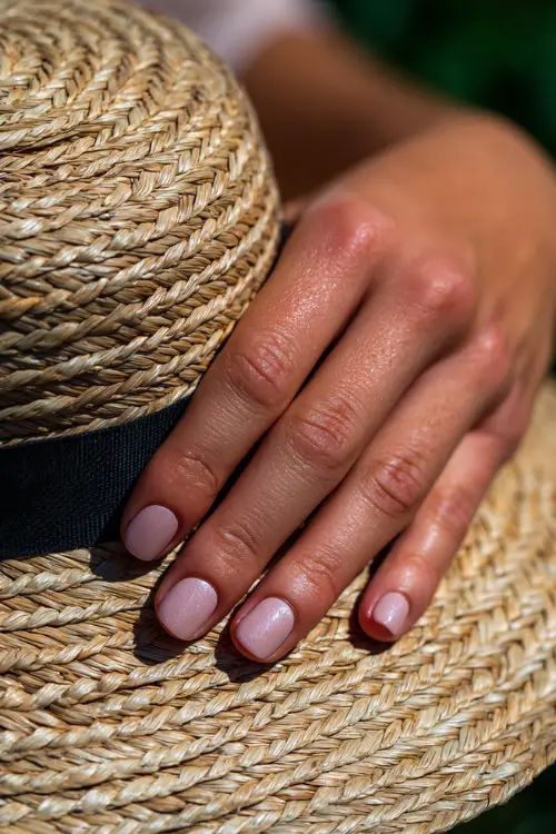 Guest’s hand resting on a straw hat, short square nails in soft blush pink with subtle silver foil on the ring fingers, perfect for an outdoor garden wedding 