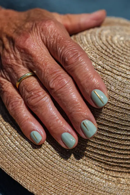 Guest’s hand resting on a woven sunhat, medium square nails painted in pastel mint green with thin gold lines and shimmer topcoat