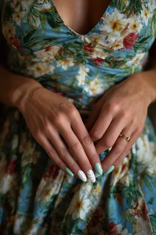 Hand adjusting floral-print dress, soft sage green nails in almond shape with clear glossy overlay and one nail in white leaf art 