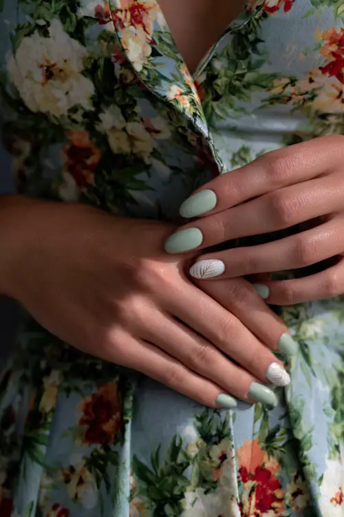 Hand adjusting floral-print dress, soft sage green nails in almond shape with clear glossy overlay and one nail in white leaf art