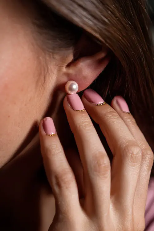 Hand adjusting pearl earring, short square nails in pastel pink with matte finish and gold dot cuticle accents