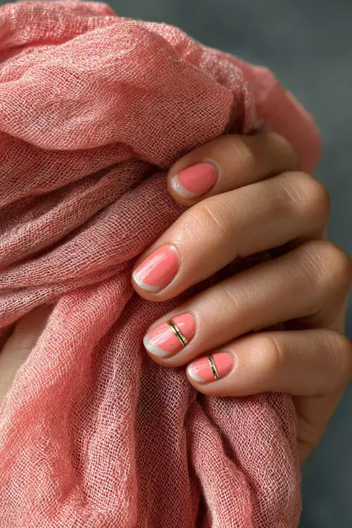 Hand gently holding sheer scarf, short nails in pale coral with transparent French tip and a tiny gold stripe across the middle 