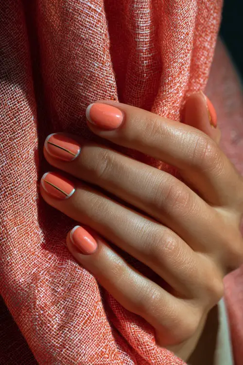 Hand gently holding sheer scarf, short nails in pale coral with transparent French tip and a tiny gold stripe across the middle 