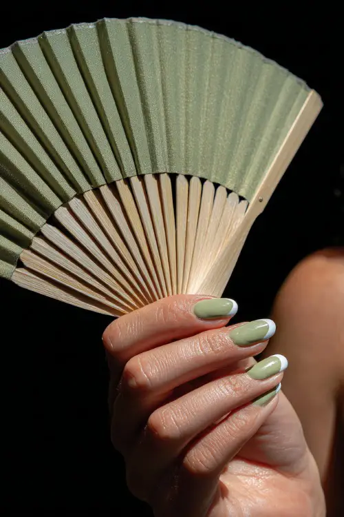 A woman holding a green fan with white nails