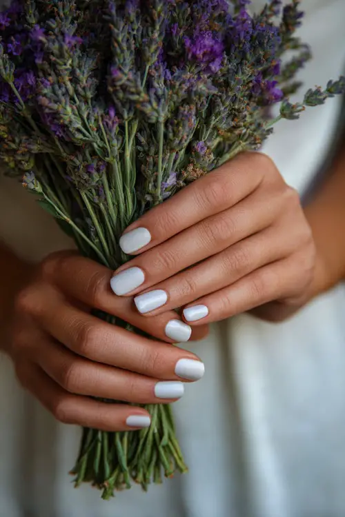 Hand of bridesmaid holding a floral bouquet, square-shaped milky white nails with tiny lavender dot accents on each nail