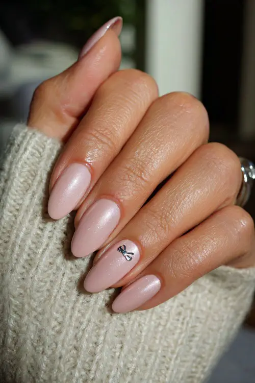 Hand resting on love note, almond-shaped nails in sheer milky pink with chrome shimmer and a delicate bow decal on the middle finger 