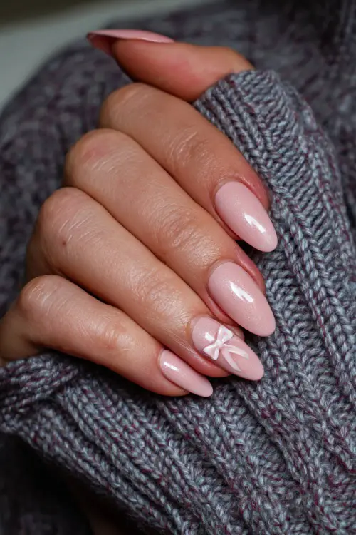 Hand resting on love note, almond-shaped nails in sheer milky pink with chrome shimmer and a delicate bow decal on the middle finger