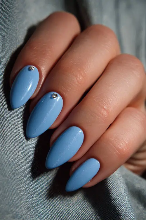 Hand tucking veil behind ear, almond nails in soft pastel blue with chrome shimmer and a single crystal stud at the base of each nail 