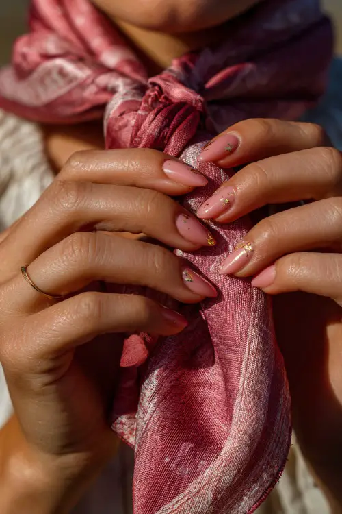 Hand tying a silk scarf, almond-shaped nails in translucent pink with gold foil flakes on ring fingers, soft summer lighting in background