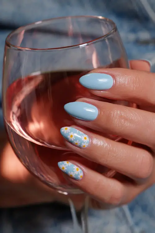 Holding a glass of rosé, almond-shaped nails in pastel blue with glossy topcoat and tiny daisy pattern across tips 