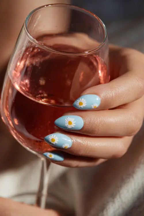 Holding a glass of rosé, almond-shaped nails in pastel blue with glossy topcoat and tiny daisy pattern across tips
