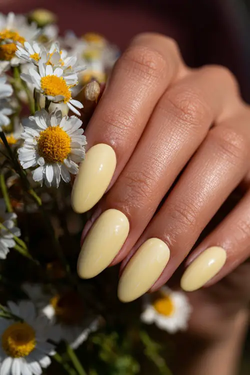 Soft close-up of bridal hand on bouquet stem, ballerina-shaped nails in pastel yellow with glossy overlay and daisy petal art on one finger 