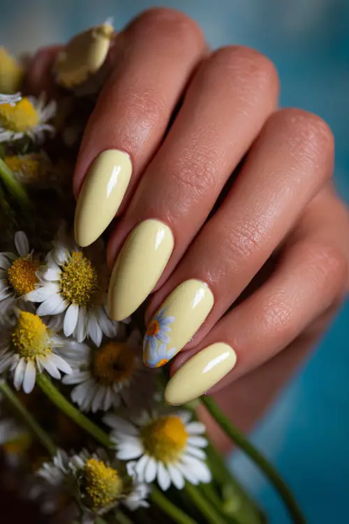 Soft close-up of bridal hand on bouquet stem, ballerina-shaped nails in pastel yellow with glossy overlay and daisy petal art on one finger 