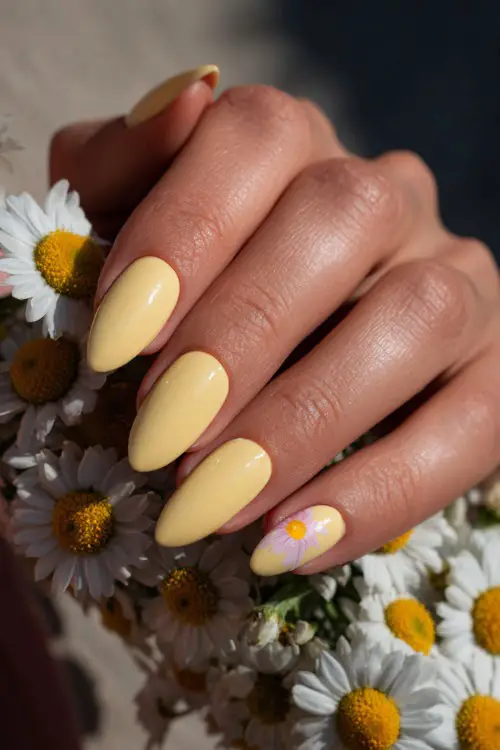 Soft close-up of bridal hand on bouquet stem, ballerina-shaped nails in pastel yellow with glossy overlay and daisy petal art on one finger 