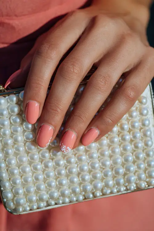 Soft close-up of bride’s hand on pearl-trimmed clutch, almond nails in pastel coral with tiny white vine design across the tips 